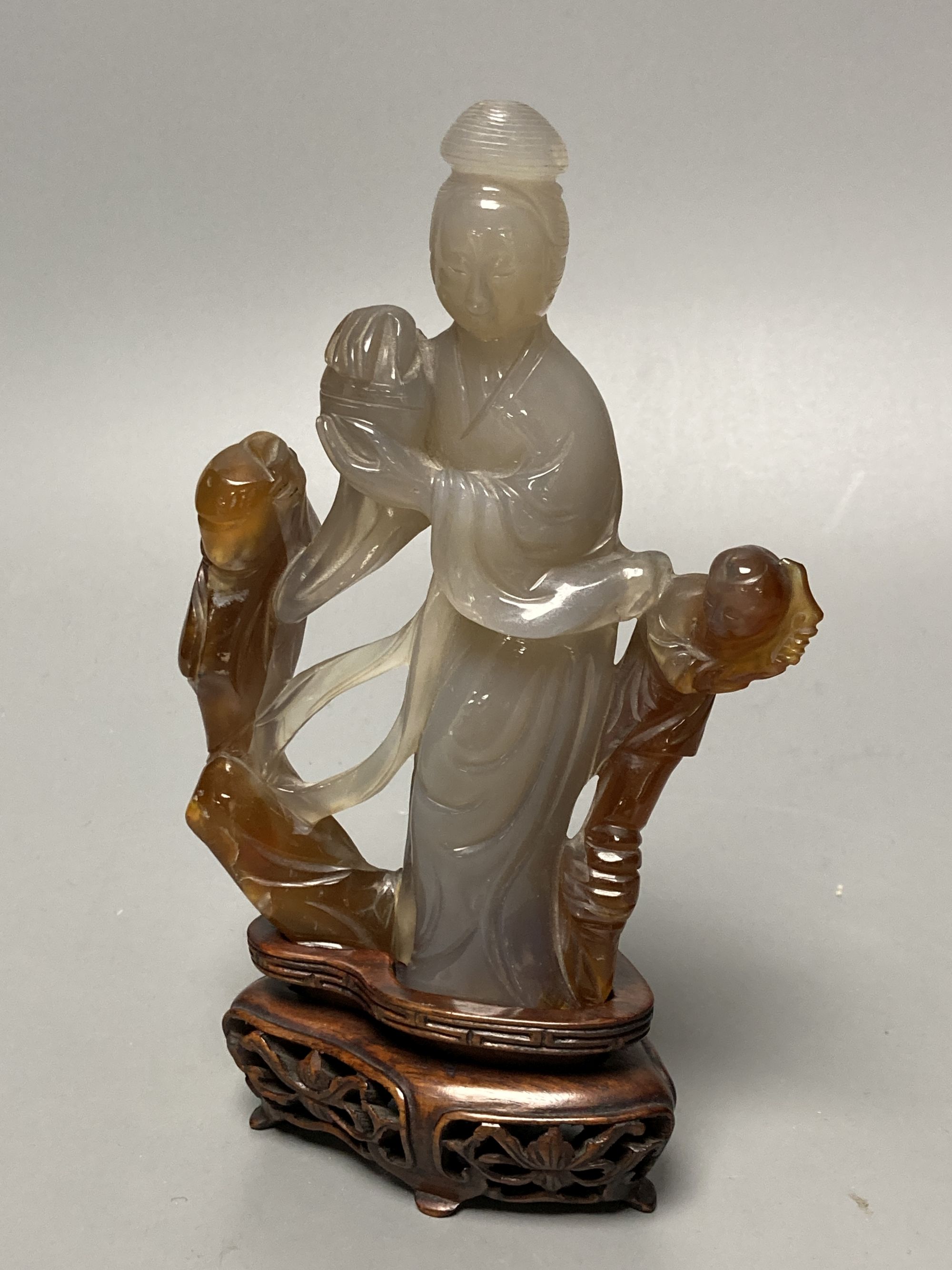 An early 20th century Chinese agate group of Guanyin and two boys, wood stand